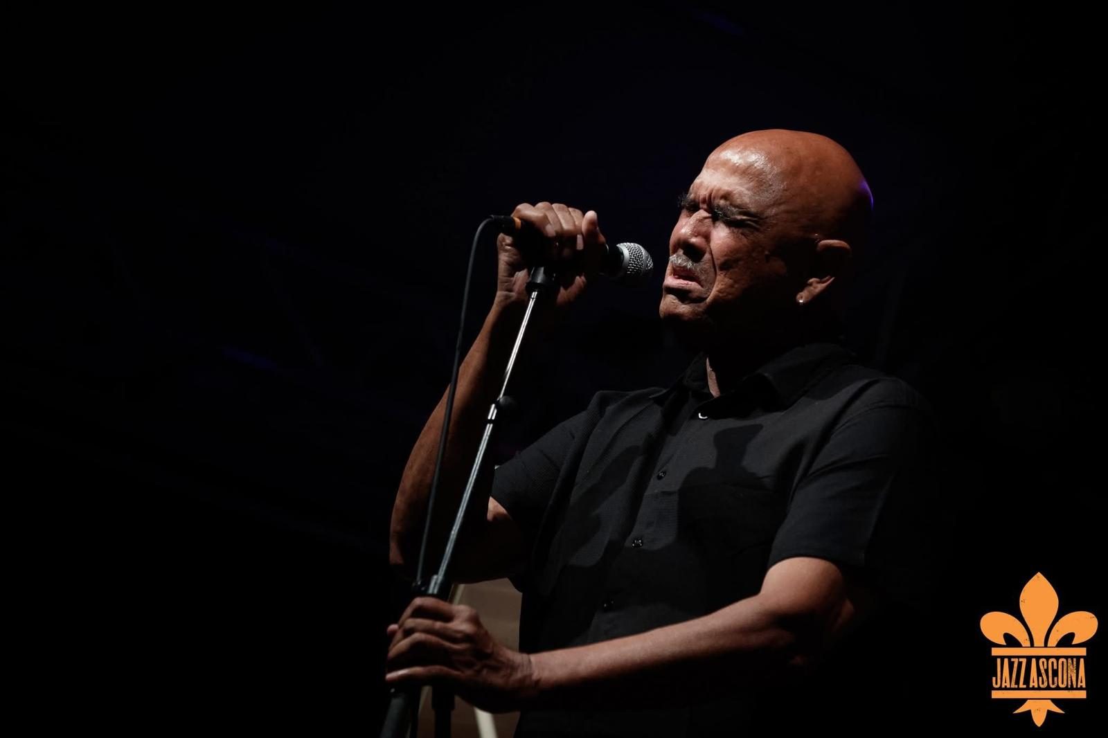 Vocalist in a black shirt singing under a single spotlight