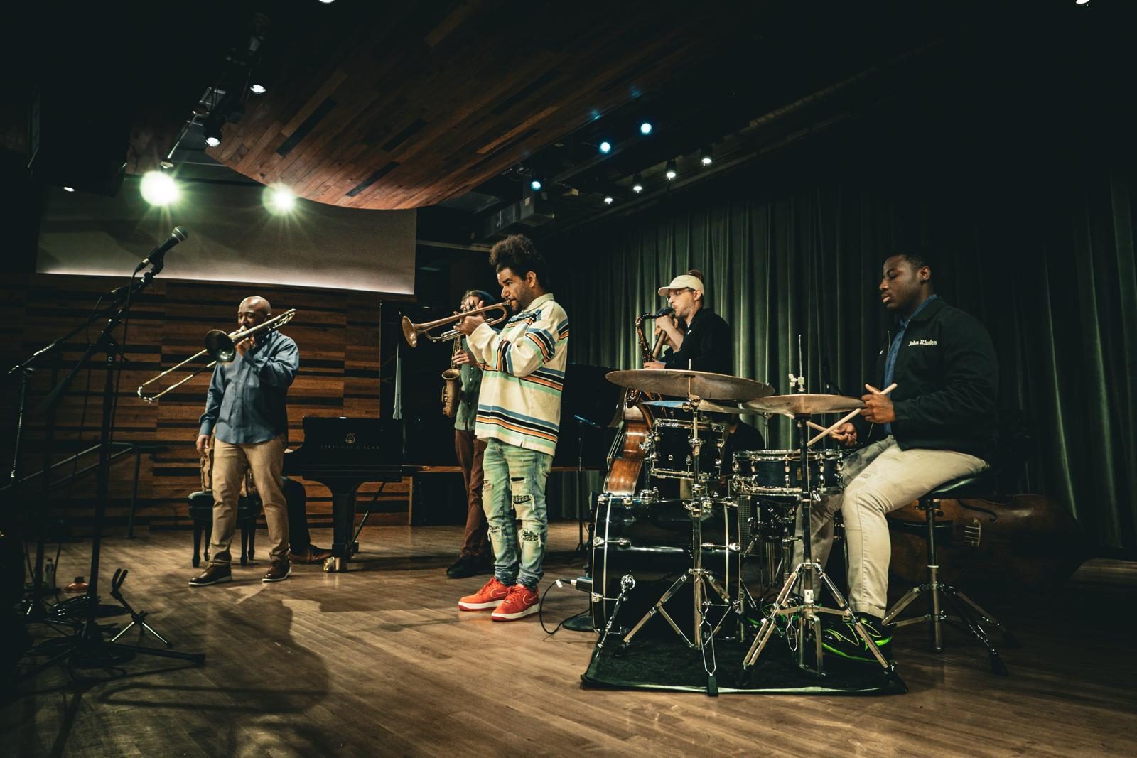 New Orleans musicians performing on trombone, trumpet, saxophone and drums on a wood-panelled stage