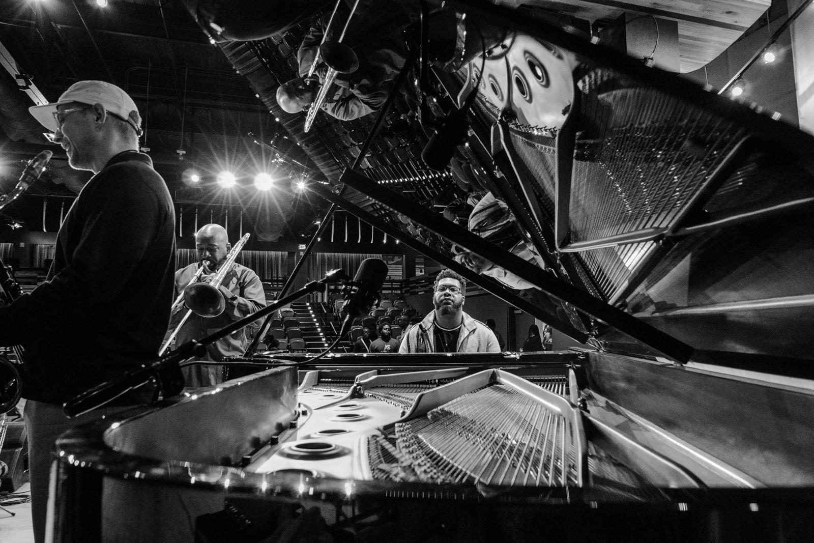 Pianist, trombonist and saxophonist rehearsing around an open grand piano