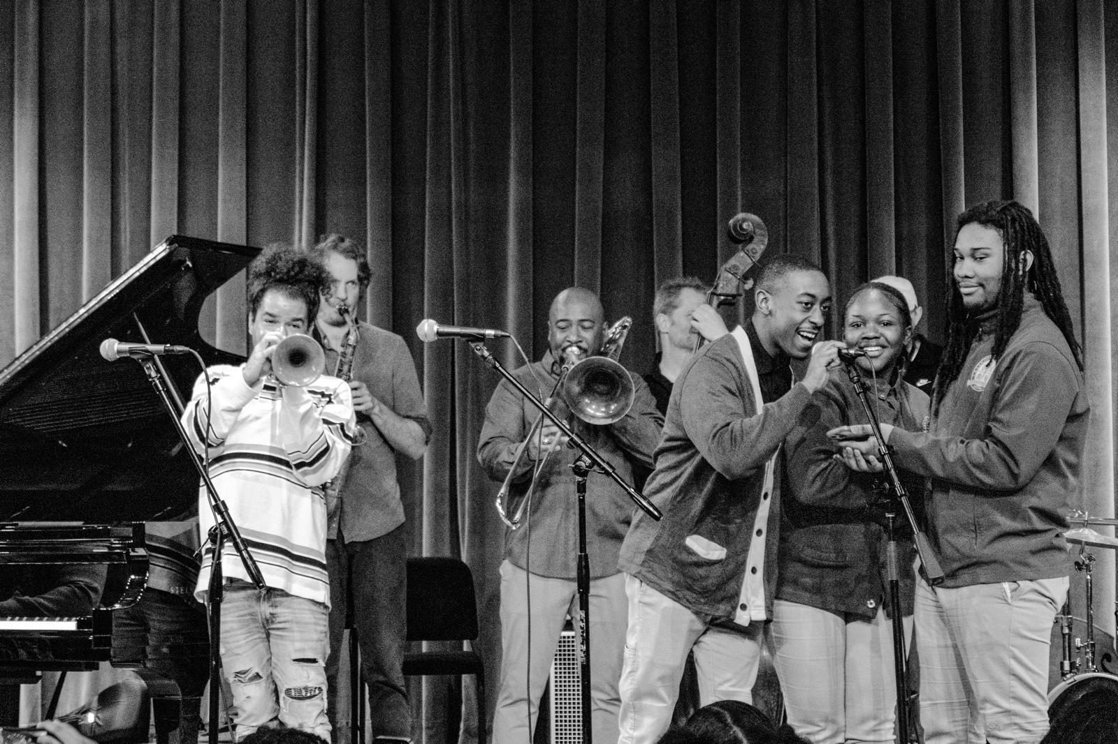 Young vocalists sharing a microphone with professional horn players on stage